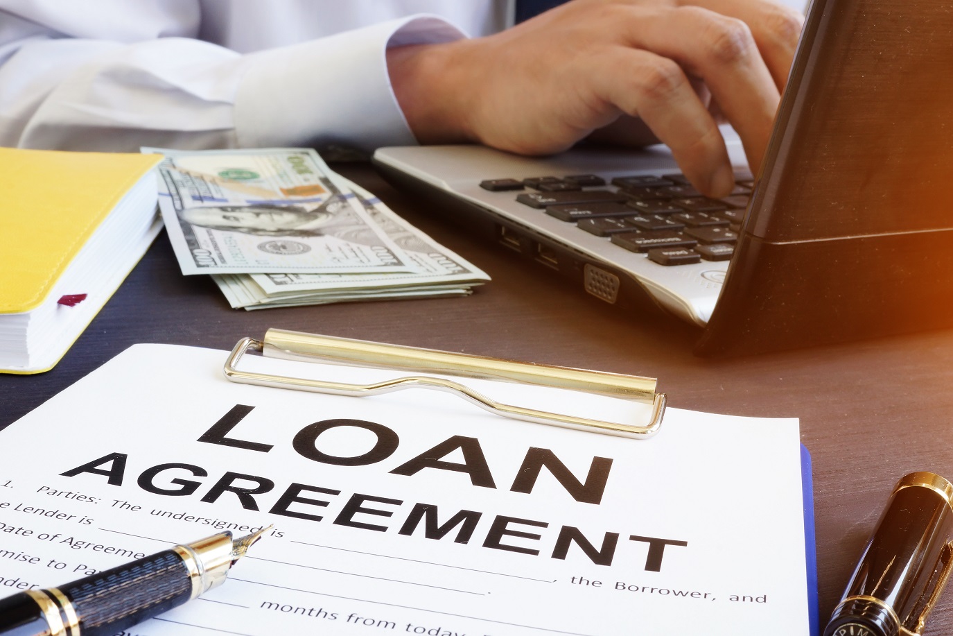 Man on Laptop with Loan Agreement on Desk